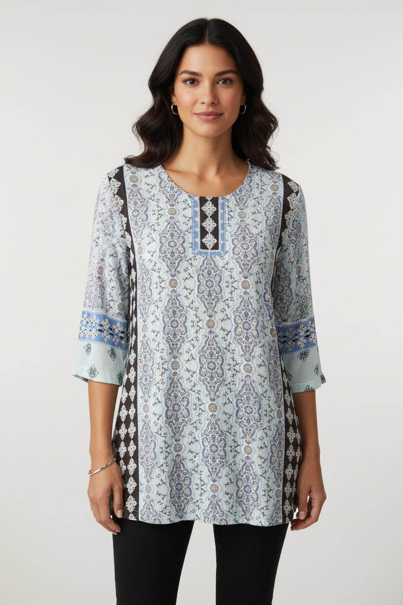 A patterned tunic top with a round neckline and vertical embroidered detailing, hanging on a beige plastic hanger on a clothing rack.